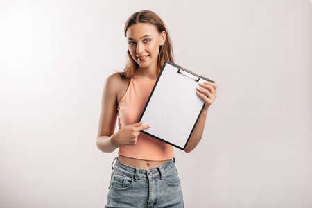 Girl student points to the sheet. Beautiful young business woman holds a clipboard with mockup blank space isolated on gray background. Study and business concept. Online learning coverの写真素材