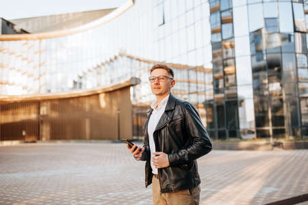 Handsome man with glasses with a smartphone on the street of a big city. Businessman talking on the phone on urban backgroundの写真素材