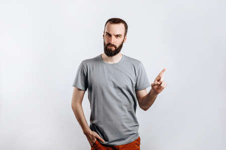 Portrait of cheerful young handsome man smiling looking at camera pointing finger upwards on white background with space for advertising mock upの写真素材