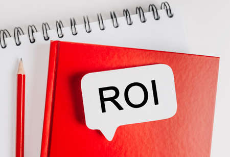 Text ROI on a white sticker with office stationery background. Flat lay on business, finance and development conceptの写真素材