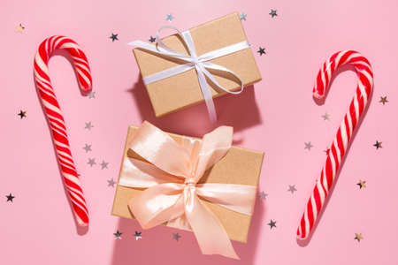 Gifts with red Christmas candies and confetti stars pours on a pastel pink background, top view. Flat lay. Holiday new year, celebration atmosphere conceptの写真素材