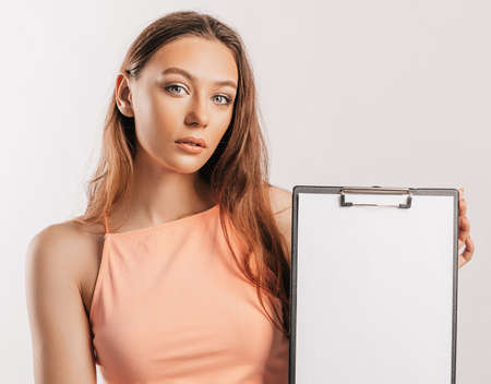 Girl student points to the sheet. Beautiful young business woman holds a clipboard with mockup blank space isolated on gray background. Study and business concept. Online learning coverの写真素材