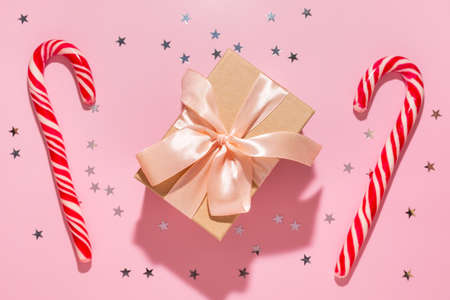 Gift with red Christmas candies and confetti stars pours on a pastel pink background, top view. Flat lay. Holiday new year, celebration atmosphere conceptの写真素材