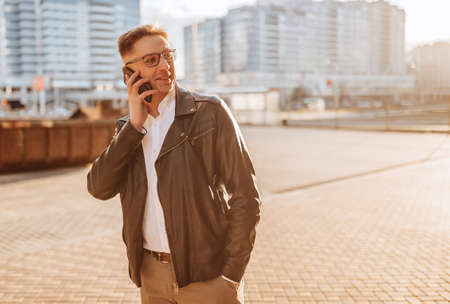 Handsome man with glasses with a smartphone on the street of a big city. Businessman talking on the phone on urban backgroundの写真素材
