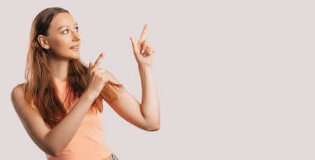 Portrait of a smiling girl pointing finger to the side at on a white isolated background. Positive woman points to an idea, a place for advertisingの写真素材