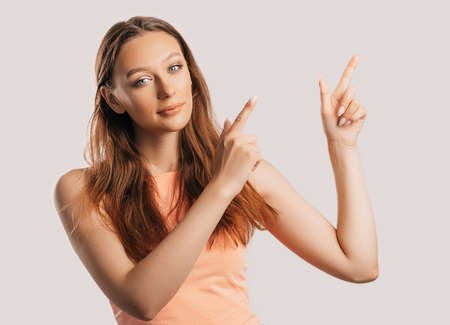 Portrait of a smiling girl pointing finger to the side at on a white isolated background. Positive woman points to an idea, a place for advertisingの写真素材