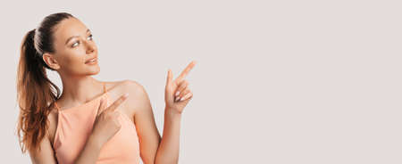 Portrait of a smiling girl pointing finger to the side at on a white isolated background. Positive woman points to an idea, a place for advertisingの写真素材