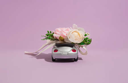Silver convertible small car model with flowers on a purple background. The concept of delivery of flowers and gifts for the holiday and celebrationの写真素材
