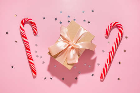 Gift with red Christmas candies and confetti stars pours on a pastel pink background, top view. Flat lay. Holiday new year, celebration atmosphere conceptの写真素材