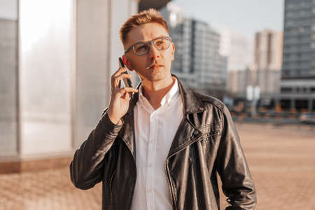 Handsome man with glasses with a smartphone on the street of a big city. Businessman talking on the phone on urban backgroundの写真素材