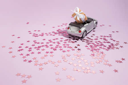 Silver convertible car carrying a gift for the holiday on a purple background. New year, christmas and Valentine conceptの写真素材
