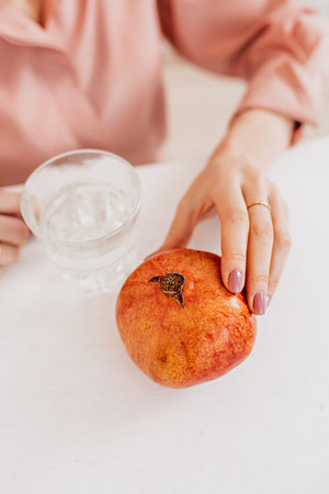 The girl is holding a pomegranate and water in the kitchen. Health care concept, dietの写真素材