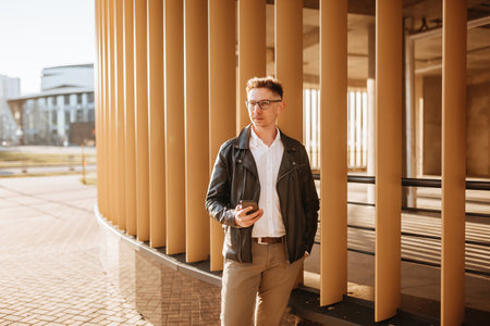 Handsome man with glasses with a smartphone on the street of a big city. Businessman talking on the phone on urban backgroundの写真素材