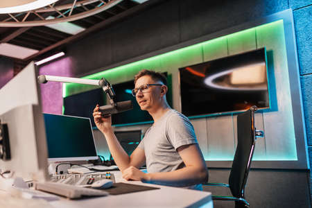 The DJ hosts the program and communicates with the audience on air at the radio station. The announcer reads the news. A male radio host speaks into a microphone and records a podcastの写真素材