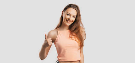 Beautiful young girl smiling and shows thumbs up gesture hand on a white isolated background. Positive woman points to an idea, a place for advertisingの写真素材