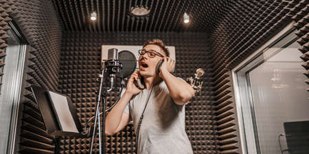 The vocalist sings in the studio in a microphone. Man in headphones writes a podcast, an audiobook. Artist, recording an album, working with the label. Announcer records a speech at a radio stationの写真素材