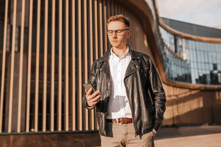 Handsome man with glasses with a smartphone on the street of a big city. Businessman talking on the phone on urban backgroundの写真素材