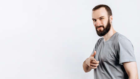 Portrait of cheerful young handsome man smiling looking at camera pointing finger forward on white background with space for advertising mock upの写真素材