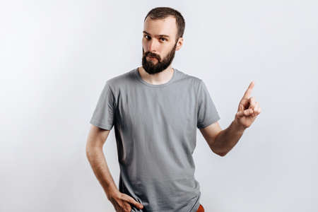 Portrait of cheerful young handsome man smiling looking at camera pointing finger upwards on white background with space for advertising mock upの写真素材