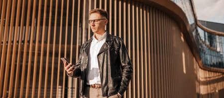 Handsome man with glasses with a smartphone on the street of a big city. Businessman talking on the...