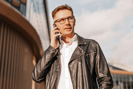 Handsome man with glasses with a smartphone on the street of a big city. Businessman talking on the phone on urban backgroundの写真素材
