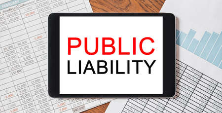 Tablet with text PUBLIC LIABILITY on your desktop with documents, reports and graphs. Business and finance conceptの写真素材