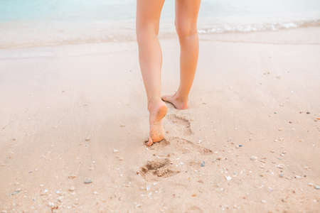 Female legs walking along the seaside barefoot, close-up of the perfect tanned legs of a girl coming out of the water after swimming. Woman relaxing on vacation, enjoying time at the beach, summer vacation conceptの写真素材