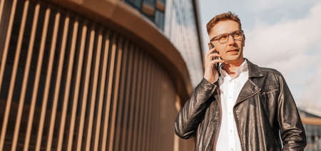 Handsome man with glasses with a smartphone on the street of a big city. Businessman talking on the phone on urban backgroundの写真素材