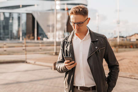 Handsome man with glasses with a smartphone on the street of a big city. Businessman talking on the phone on urban backgroundの写真素材