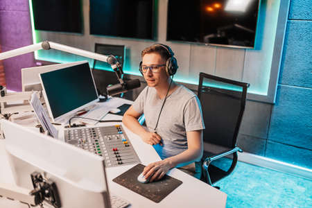 The DJ hosts the program and communicates with the audience on air at the radio station. The announcer reads the news. A male radio host speaks into a microphone and records a podcastの写真素材