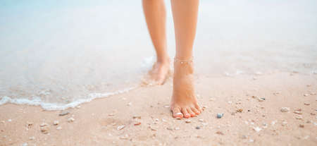 Female legs walking along the seaside barefoot, close-up of the perfect tanned legs of a girl coming out of the water after swimming. Woman relaxing on vacation, enjoying time at the beach, summer vacation conceptの写真素材