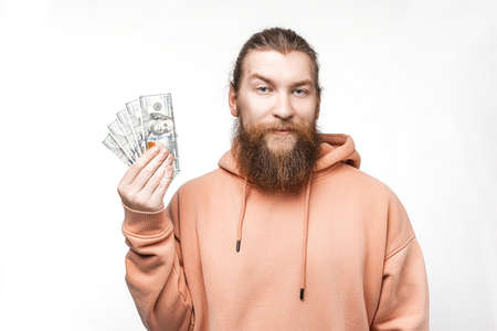 Handsome scandinavian man holding dollar currency money in his hands on gray background. Guy with ginger hairstyle and beard in a sweatshirt. The concept of money, salary, finance, investmentの写真素材