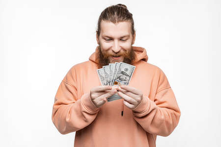 Handsome scandinavian man holding dollar currency money in his hands on gray background. Guy with...