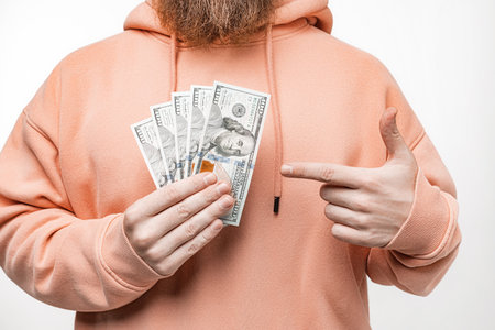 Man holding dollar currency money in his hands. Guy have cash in a pink or orange sweatshirt. The concept of money, salary, finance, investmentの写真素材