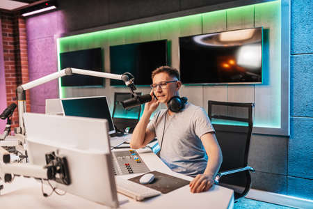 The DJ hosts the program and communicates with the audience on air at the radio station. The announcer reads the news. A male radio host speaks into a microphone and records a podcastの写真素材