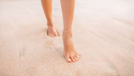 Female legs walking along the seaside barefoot, close-up of the perfect tanned legs of a girl coming out of the water after swimming. Woman relaxing on vacation, enjoying time at the beach, summer vacation conceptの写真素材