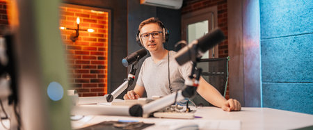 The DJ hosts the program and communicates with the audience on air at the radio station. The announcer reads the news. A male radio host speaks into a microphone and records a podcastの写真素材