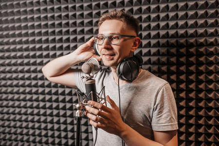 The vocalist sings in the studio in a microphone. Man in headphones writes a podcast, an audiobook. Artist, recording an album, working with the label. Announcer records a speech at a radio stationの写真素材