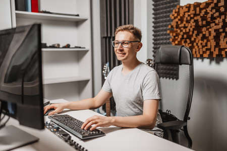 Man working in music studio using computer wearing glasses. Sound engineer working and mixing track. Programmer watching at display of it while listening music. Technology conceptの写真素材