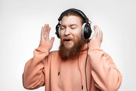 Scandinavian handsome surprised man laughs and listens to music in professional headphones isolated on gray background. Happy guy with ginger hairstyle, beard. Modern digital technologiesの写真素材