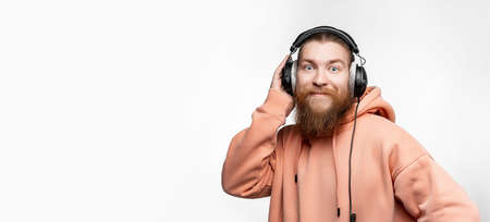 Scandinavian handsome surprised man looks to the camera and listens to music in professional headphones isolated on gray background. Happy guy with ginger hairstyle, beard. Modern digital technologiesの写真素材