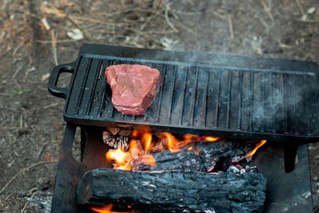 Beef steaks grilling on a cast iron plate on a camp fire. Campfire cooking. Outdoor BBQの写真素材