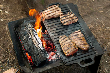 Beef steaks grilling on a cast iron plate on a camp fire. Campfire cooking. Outdoor BBQ. Selective focusの写真素材