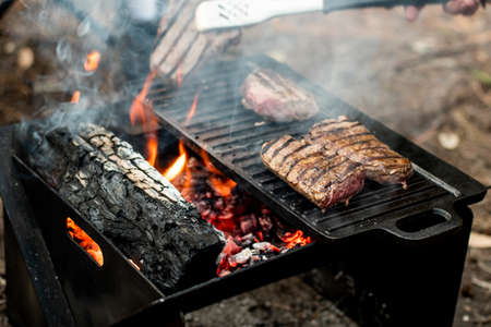 Beef steaks grilling on a cast iron plate on a camp fire. Campfire cooking. Outdoor BBQ. Selective focusの写真素材