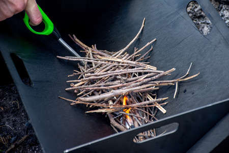 Starting the camp fire with kindling and lighter in a portable foldable firepit