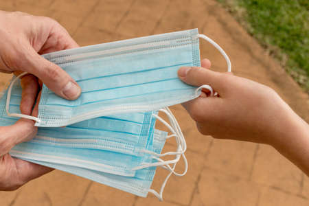 Hands holding and giving protective disposable face mask to another person. Concept of virus deseases and coronavirus COVID-19の写真素材