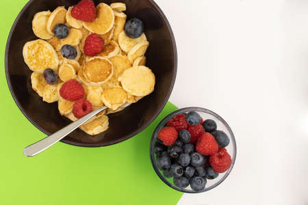 A bowl with mini pancake cereal. Trendy food. Tiny cereal pancakes with blueberries and raspberries. Copy spaceの写真素材
