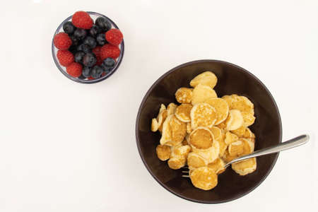 A bowl with mini pancake cereal. Trendy food. Tiny cereal pancakes with blueberries and raspberries. Copy space.の写真素材