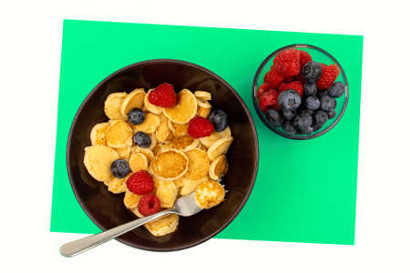 A bowl with mini pancake cereal. Trendy food. Tiny cereal pancakes with blueberries and raspberriesの写真素材