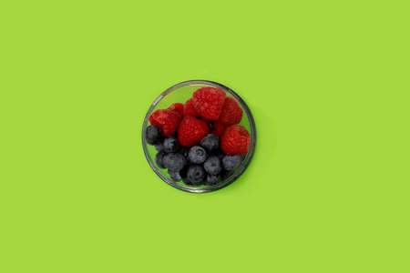 Blueberries amd raspberries in a transparent bowl on a green background. Healthy lifestyle conceptの写真素材